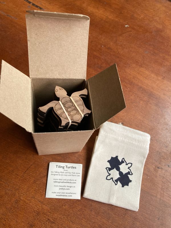 a box of wooden tiling turtles on a dark wood background, with informational insert and a canvas bag in the background.