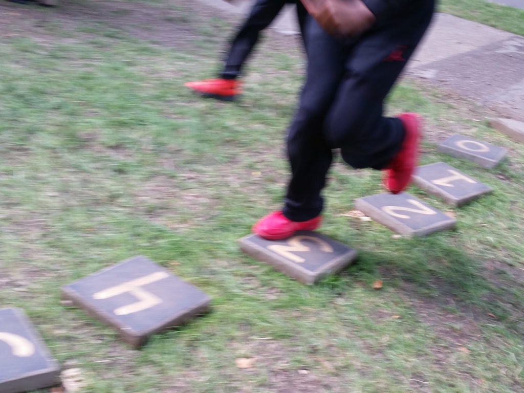 Two young people in black jeans and red sneakers hopping on numbered stepping stones.