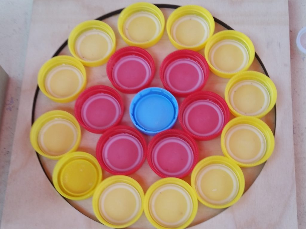 Colorful bottle caps arranged inside a wooden circle frame, resembling a flower.