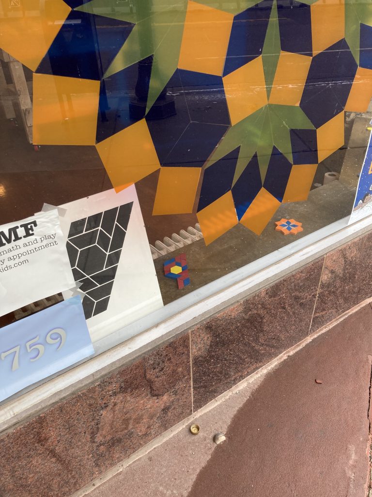 Detail of the larger window. We now see a smaller poster with black pattern blocks arranged in a fist that reminds of a Black Lives Matter logo. The same arrangement, with traditionally colored pattern blocks is on the windowsill inside.