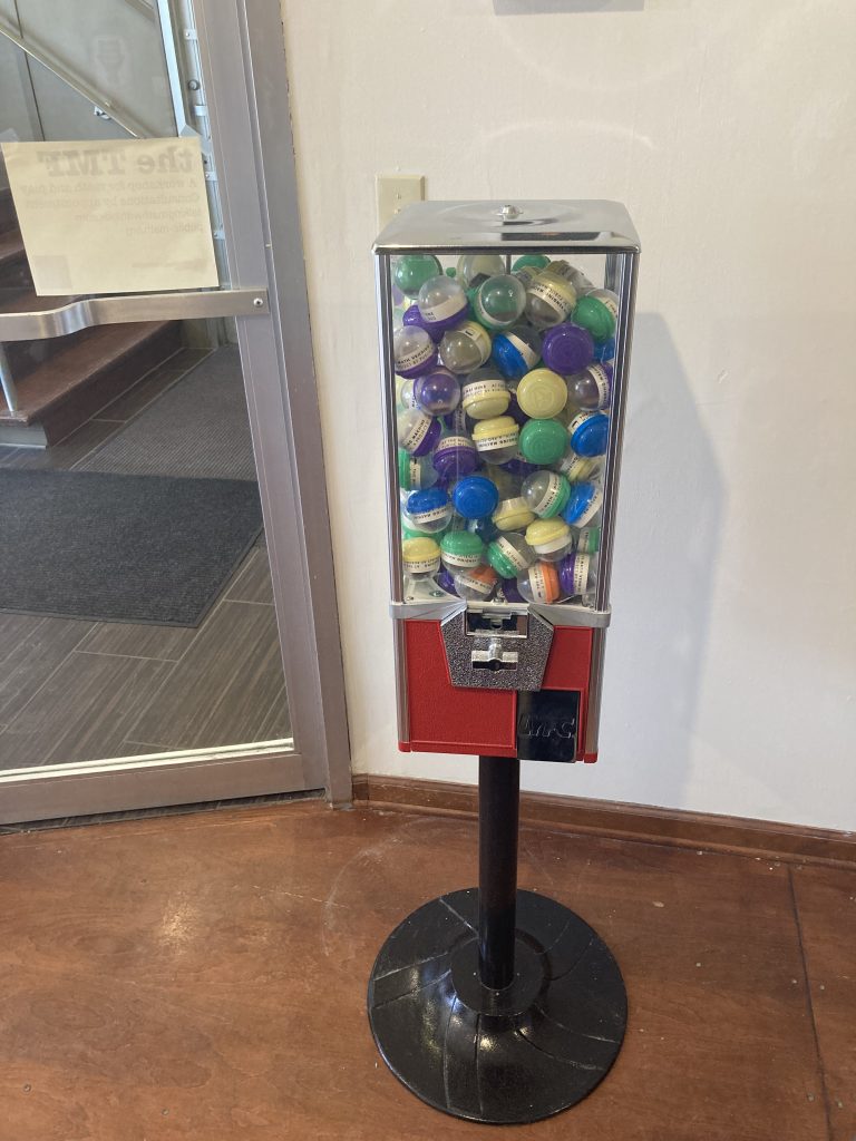 A capsule-dispensing vending machine; the kind where you insert a token, twist a handle, and the capsule drops down behind a small metal door.