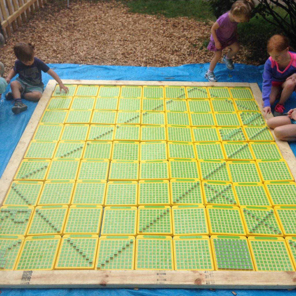 Enormous grid of 9 rows of 9 Pattern Machines laid out on the ground. Four children are kneeling and working on various parts, including one child who has made a huge rectangle at an oblique angle that hits all four edges of the mega pattern machine