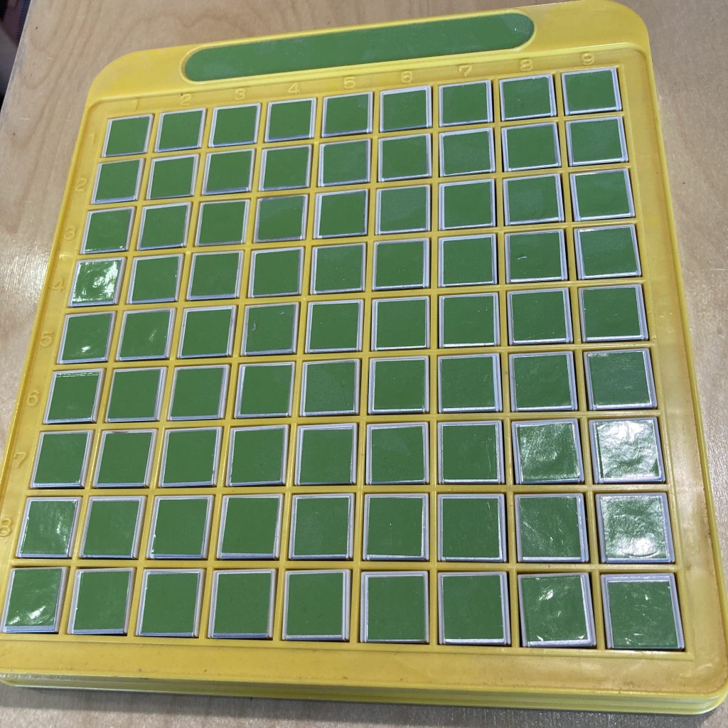 A yellow plastic rectangle with a 9 by 9 grid of blank green squares.