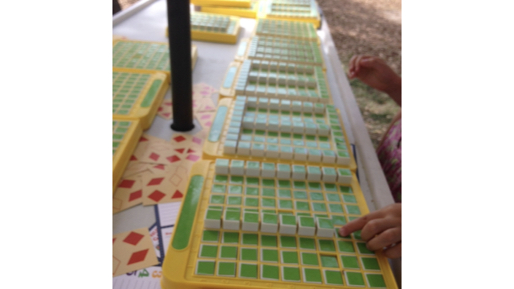 A child pushes a button on a Pattern Machine. There are several pattern machines on the table; each with one or more rectangular areas outlined with up buttons, and down buttons within.