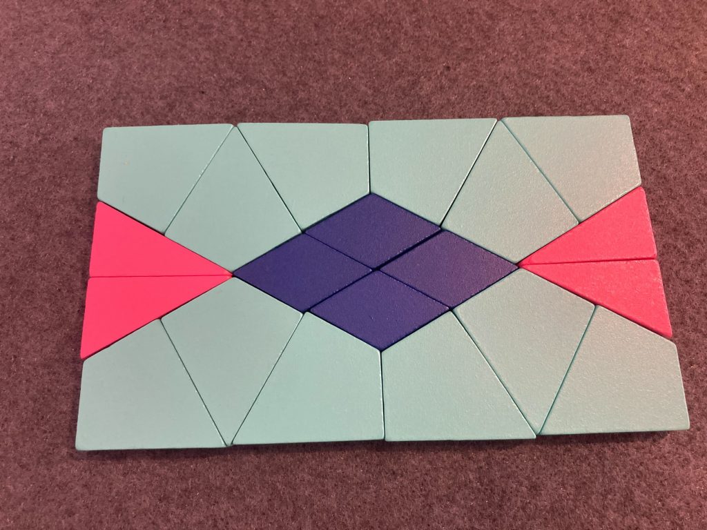 A rectangle made of 12 teal-colored kites, four pink right triangles, and four blue diamonds in an arrangement that has both horizontal and vertical lines of symmetry.