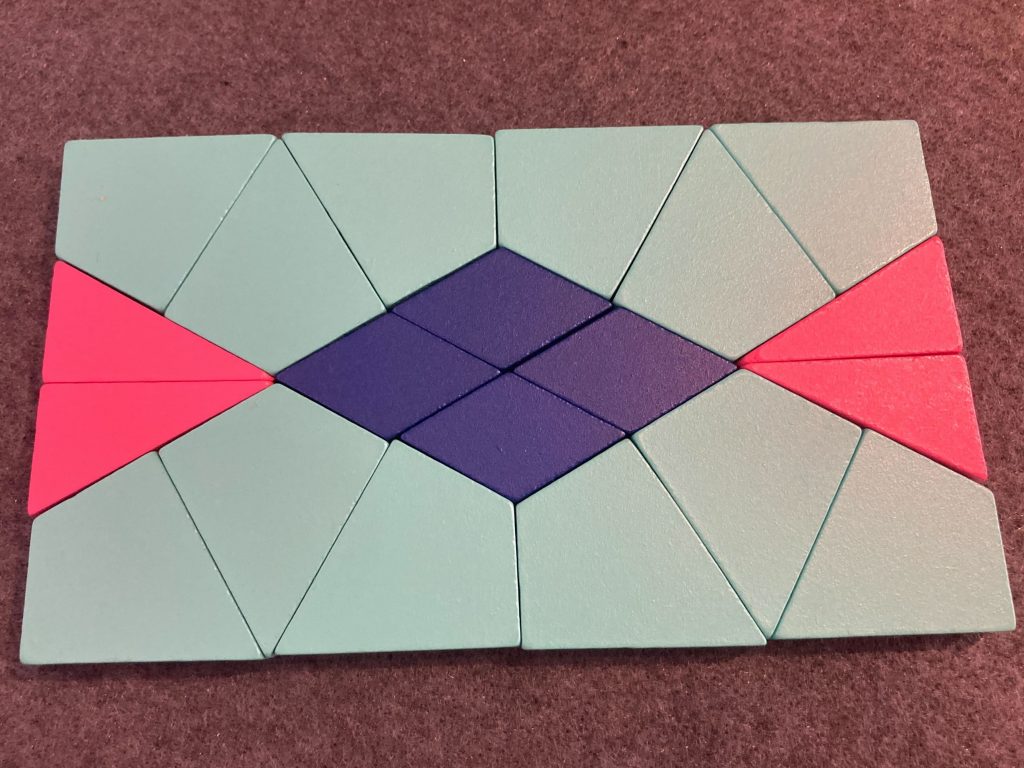 A rectangle made of 12 teal-colored kites, four pink right triangles, and four blue diamonds in an arrangement that has both horizontal and vertical lines of symmetry.