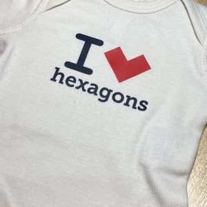 An off-white baby bodysuit that reads "I *heart* hexagons" but where the heart is actually a red, concave hexagon standing on a vertex.