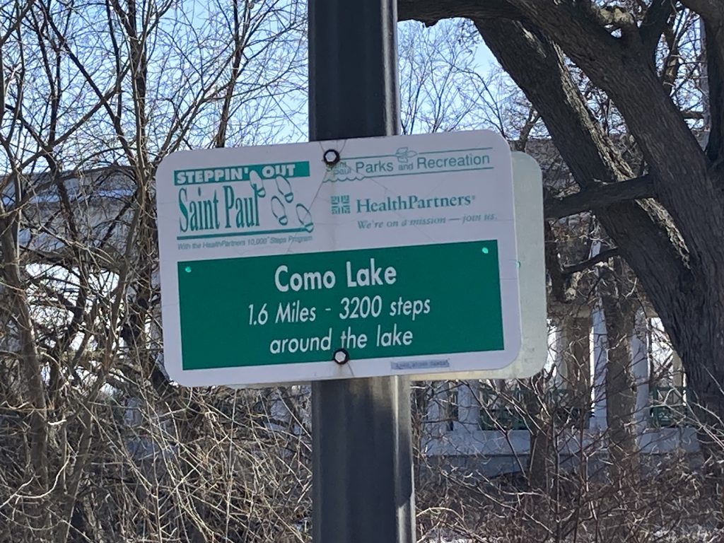 A sign on a light pole reads "Como Lake. 1.6 miles - 3200 steps around the lake"