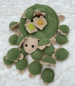 Several small crocheted turtles are arranged around a larger one. The little ones have different colors on their bellies, which allows for a game of memory. 