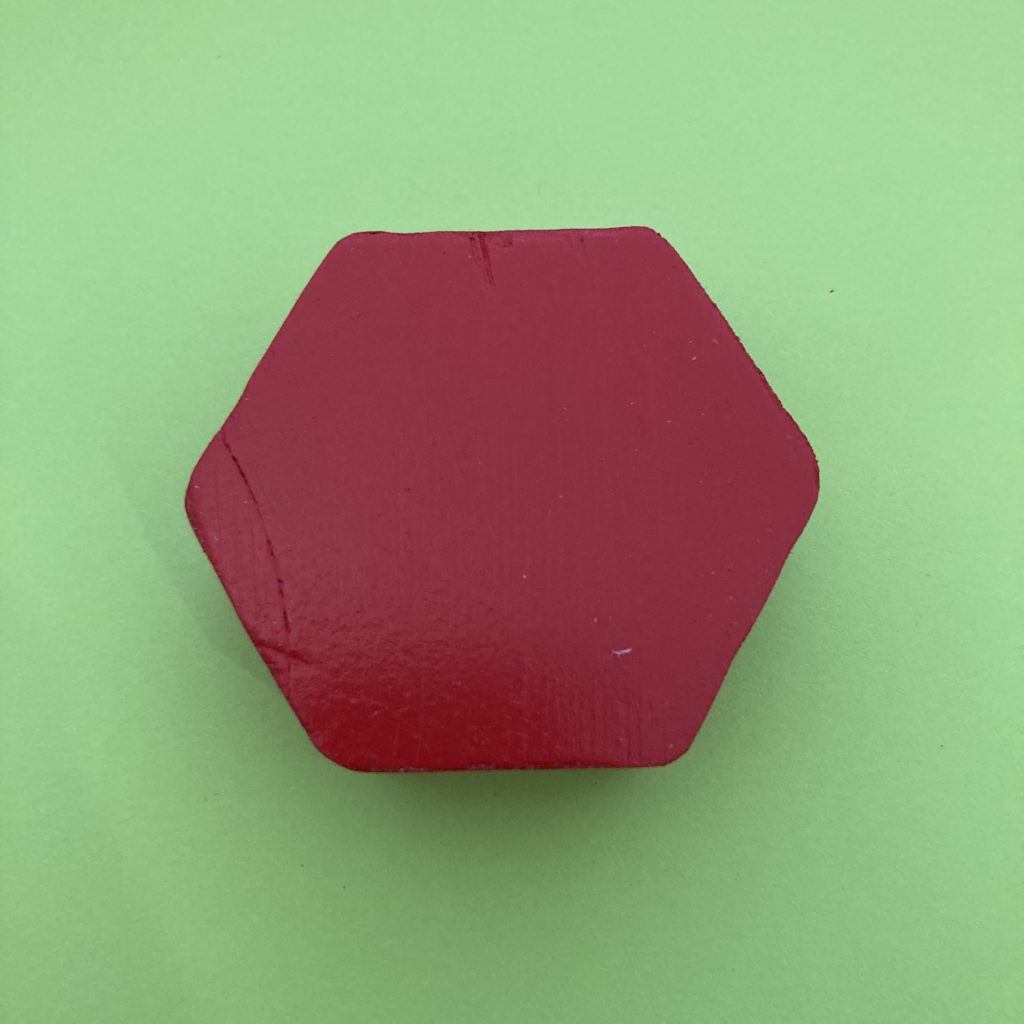 A red wooden, regular hexagon on a green background. 