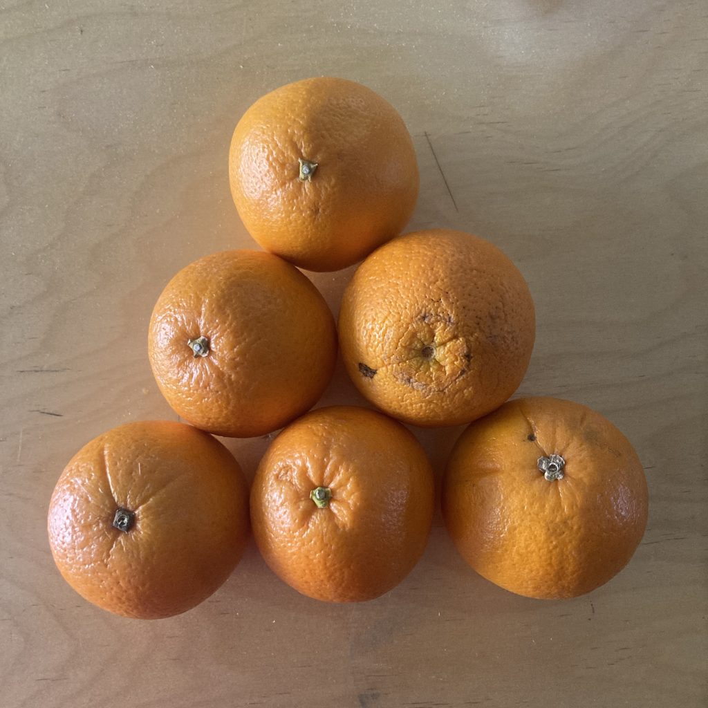 A triangle of oranges, shot from directly overhead. A row of three across the bottom, then a row of two, and then one last orange on top.