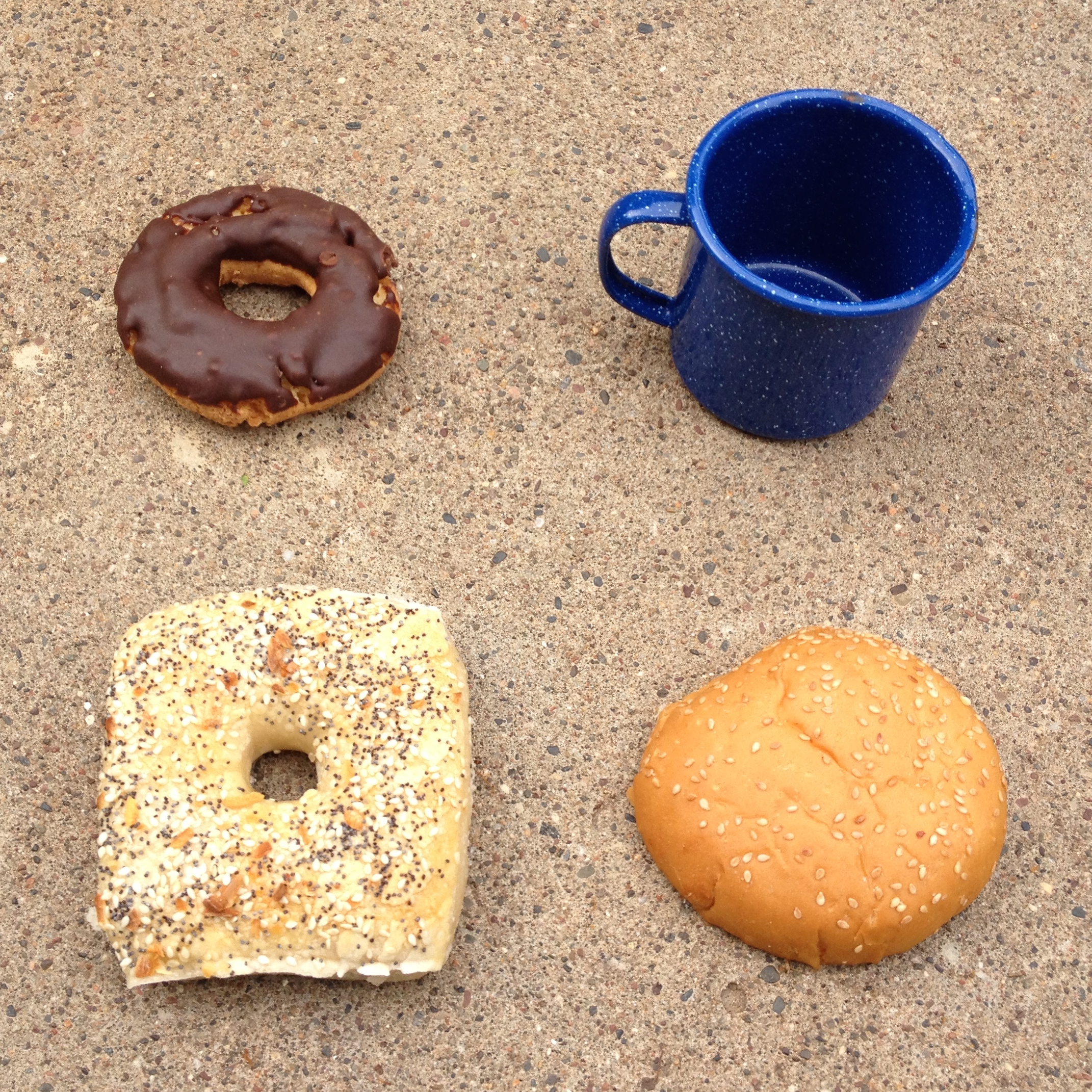 Four objects in a two-by-two grid<br />
upper left: a chocolate frosted, plain donut.<br />
upper right: a blue and white speckled metal coffee cup.<br />
lower left: a square everything bagel.<br />
lower right: the top of a hamburger bun, with sesame seeds sprinkled on top.